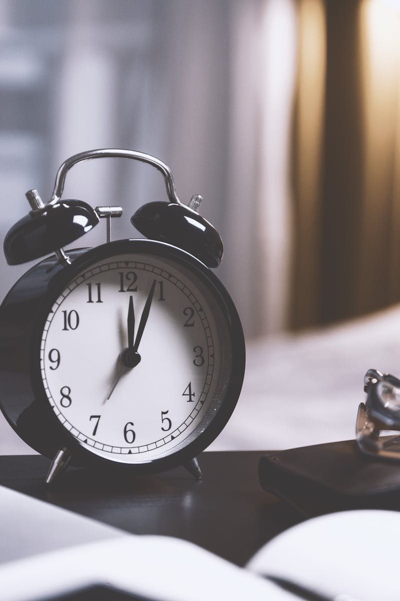 A classic analog alarm clock on a modern desk setup with a laptop and pens, creating a balanced workspace vibe.