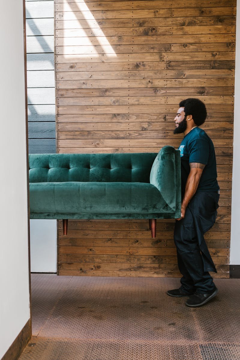 A mover carries a green sofa indoors, showcasing modern interior design and relocation services.